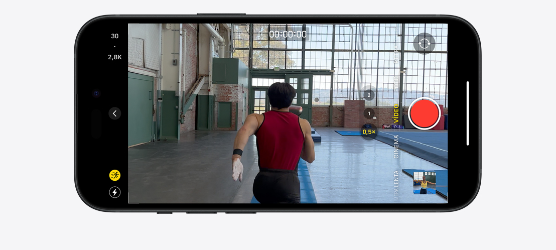 Imagem de um iPhone 15 Pro gravando um vídeo no modo Ação de um ginasta correndo em um ambiente amplo e iluminado.