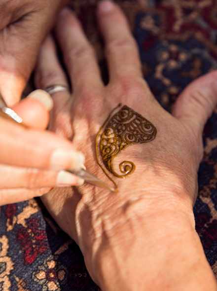 Close-up photo of one person’s hands applying a henna tattoo to another person’s hands.