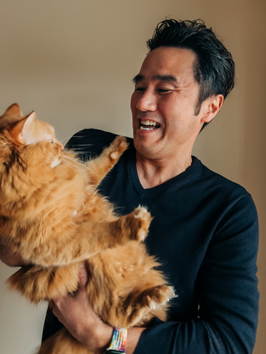 抱いている猫に笑顔を向けているテツのポートレート写真。