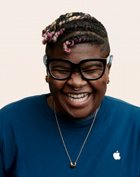 Funcionária da Apple Retail com lenço na cabeça e óculos sorrindo para a câmera. 