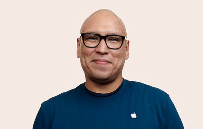 Empleada de Apple Retail con lentes negros sonríe a la cámara.