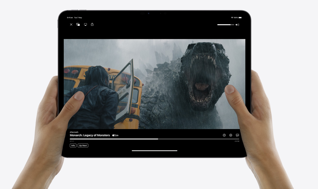Dvě ruce drží iPad Pro, na kterém je v aplikaci Apple TV puštěný seriál „Monarch: Odkaz monster“.