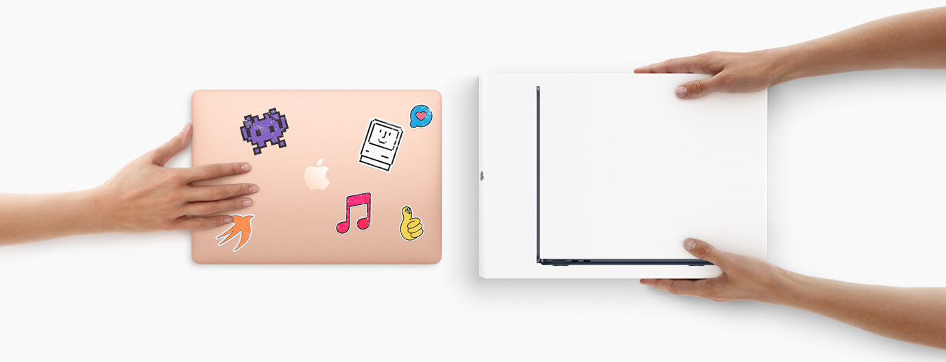 一隻手將一部外殼貼有貼紙的 MacBook 滑向前方,另一邊有兩隻手拿著全新盒裝的 MacBook