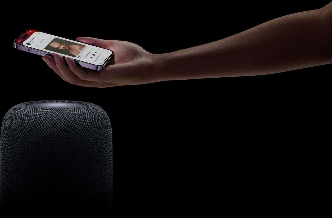 A hand coming in from the right side of the page holds an iPhone above a HomePod speaker