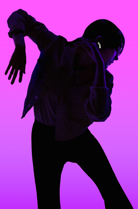 Siluetti henkilöstä, joka tanssii oikea käsi koukistettuna alaspäin ja vasen käsi koukistettuna ylöspäin, kasvoihin heijastuu violetti taustavalo korostaen oikean AirPods-korvanapin napakkaa istuvuutta korvassa.