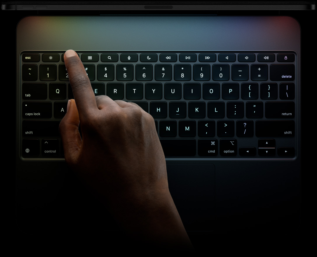 横向きのiPad Pro、上部の側面からの外観、カラーはスペースブラック。Magic Keyboardを取りつけた状態、前面の外観、横向き。ブラックカラーのバックライトキー、専用のファンクションキー列。escapeキー、tabキー、caps lockキー、shiftキー、controlキー、optionキー、shiftキー、deleteキー、returnキー、逆T字型の矢印キー、内蔵トラックパッド