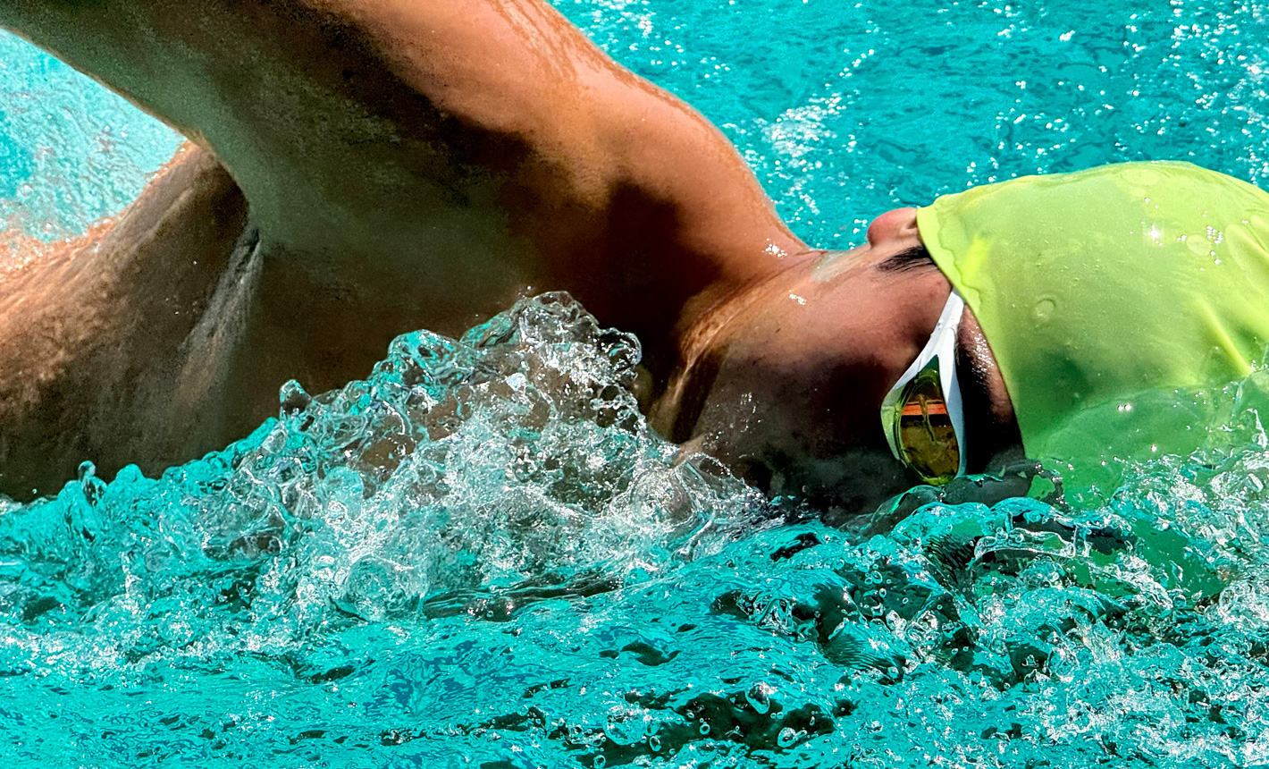 O fotografie foarte detaliată, mărită, a unui înotător într-o piscină, cu stropi de apă în jurul său