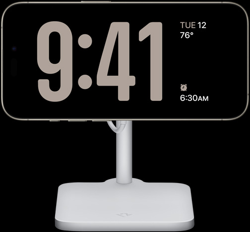 Een iPhone 15 Pro in Stand-by-modus met een schermvullende klok waarop ook de datum, de temperatuur en de wektijd te zien zijn