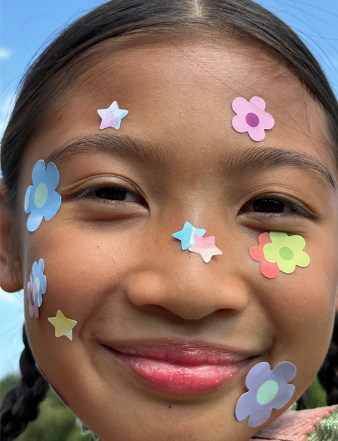 Ultra-close‑up van een meisje met bloemenstickers op haar gezicht, gemaakt met de functie voor traploos zoomen op iPhone 15