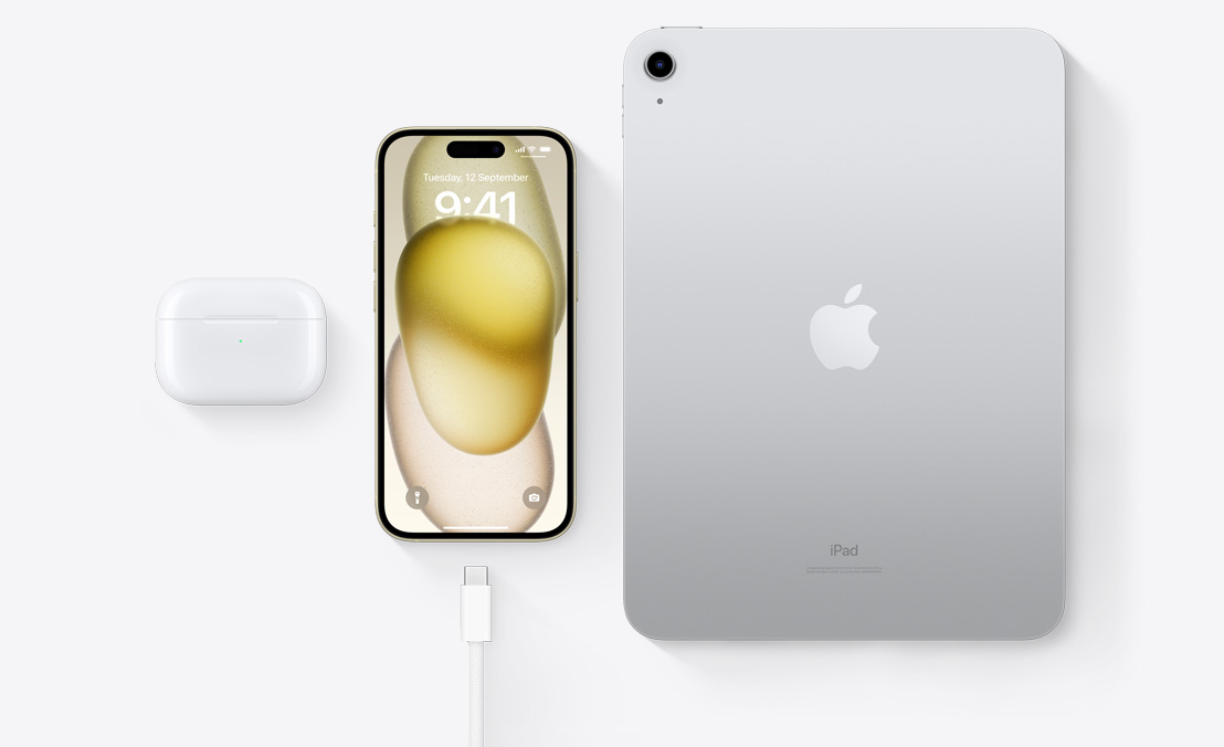 A birds-eye view of AirPods Pro, iPhone 15 and an iPad with a USB-C connector to demonstrate how all three devices can be charged using the same USB-C cable.