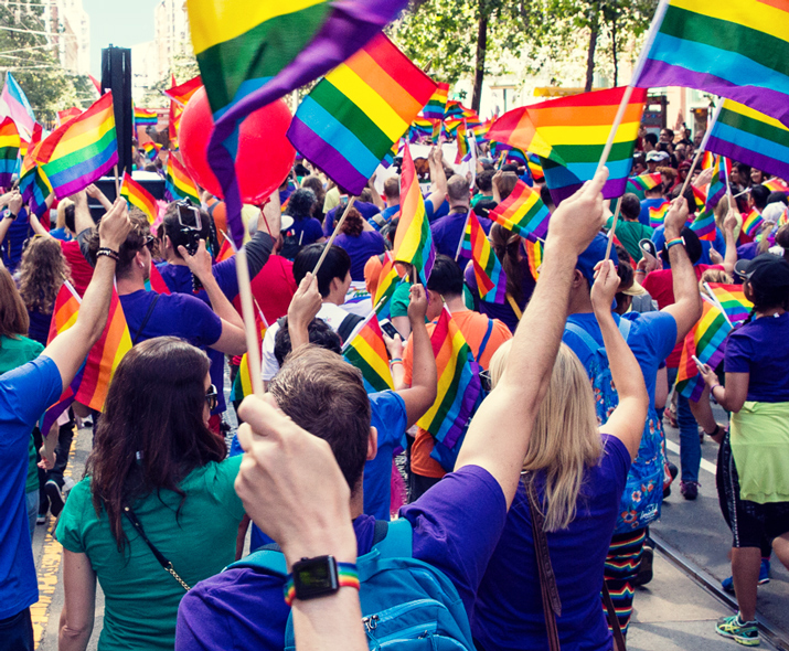 Foto de un grupo de gente en un desfile ondeando banderas de arcoíris.  