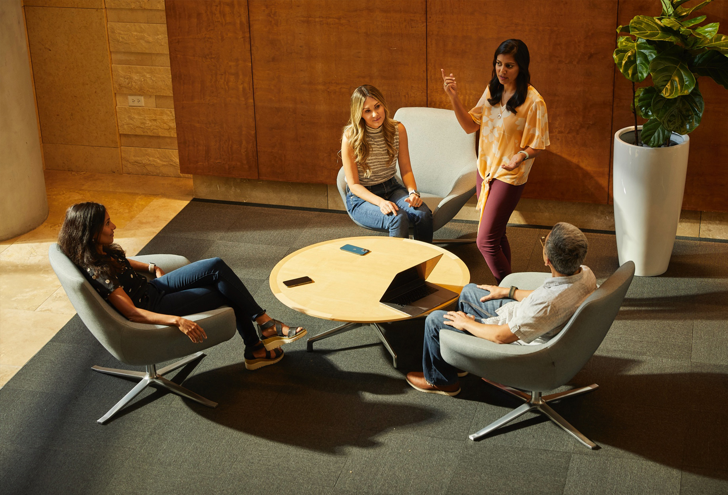 Czworo pracowników Apple siedzących i rozmawiających w komfortowej przestrzeni sprzyjającej współpracy.