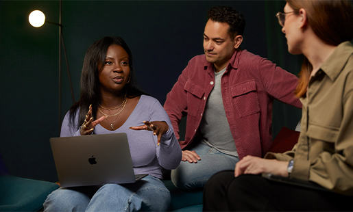 Ginelle with a MacBook on her lap, sitting and working with two colleagues.