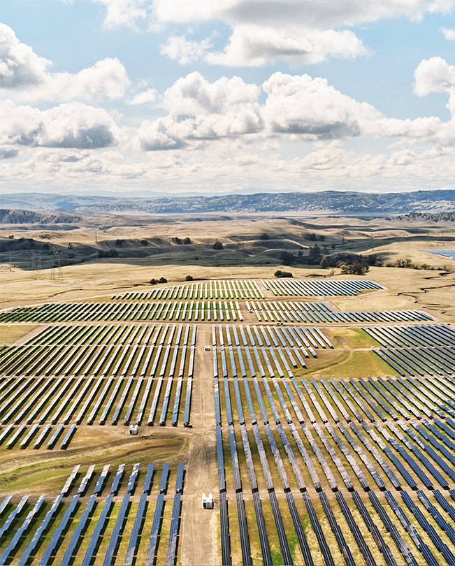 Letecký pohled na rozlehlou pláň posetou solárními panely vyrábějícími energii.