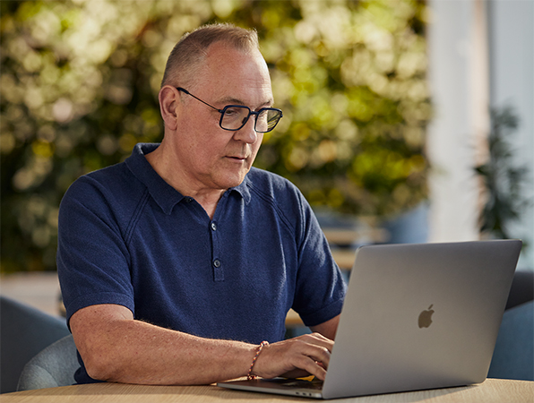 En medarbejder fra Apples Software og tjenester-team sidder udenfor og arbejder på en MacBook med et grønt område i baggrunden.