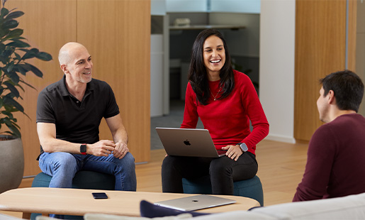 Camila rindo com um MacBook no colo, junto com dois colegas da Apple.