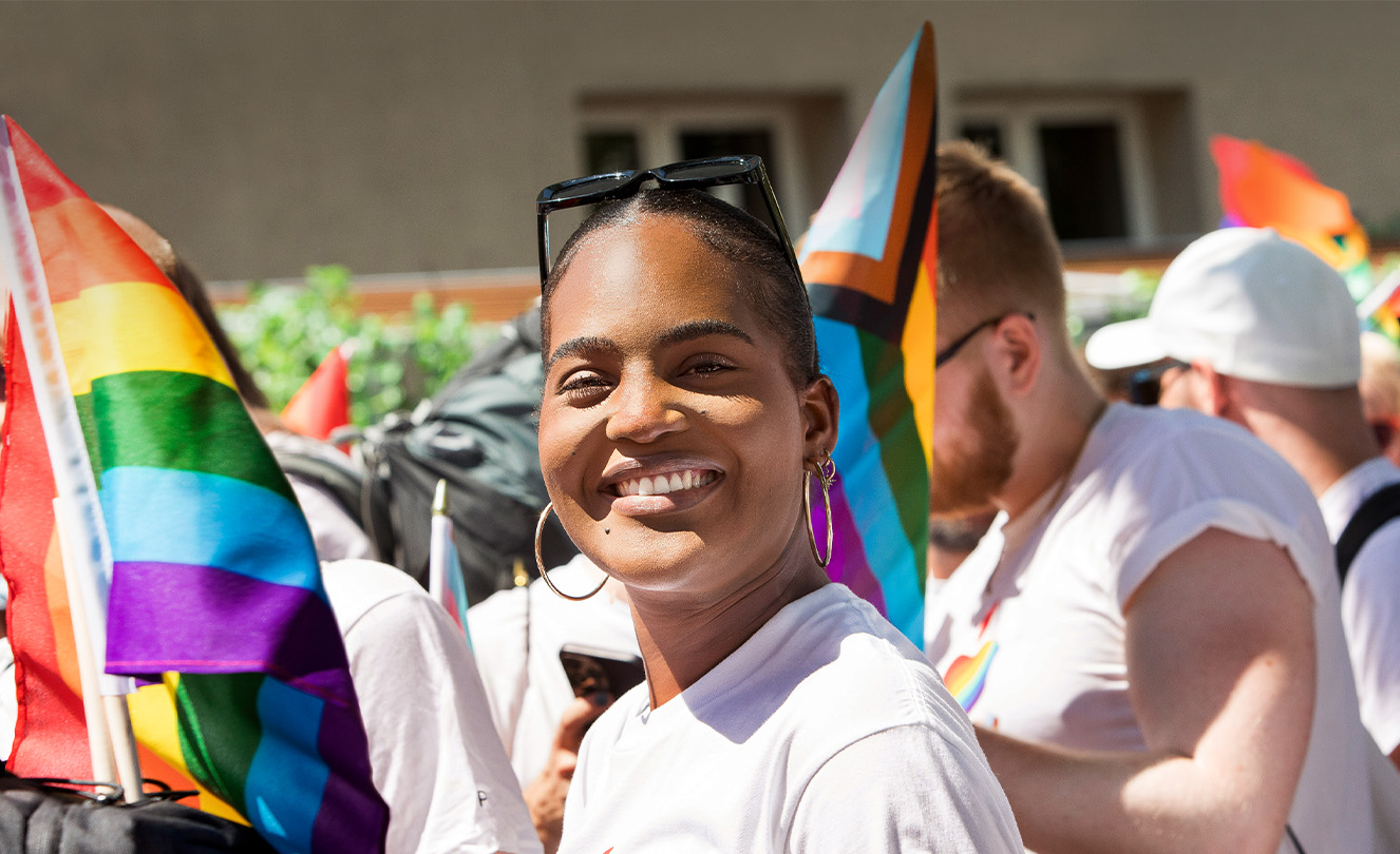 En leende Apple-medarbetare vid ett Apple prideevent bland andra medarbetare som håller prideflaggor och bär pridetröjor 