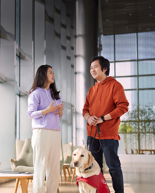 Aydınlık bir ortak alanda konuşan iki Apple çalışanından biri elinde rehber köpeğinin tasmasını tutuyor.