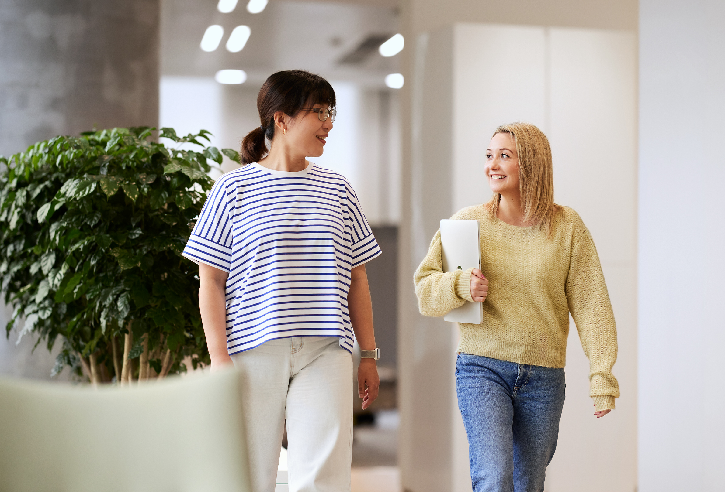 Dos empleadas de Apple sonríen y tienen una conversación mientras caminan en un espacio común iluminado.