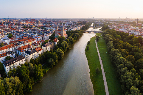 Légi felvétel Münchenről egy folyóval, fákkal és folyóparti sétánnyal.