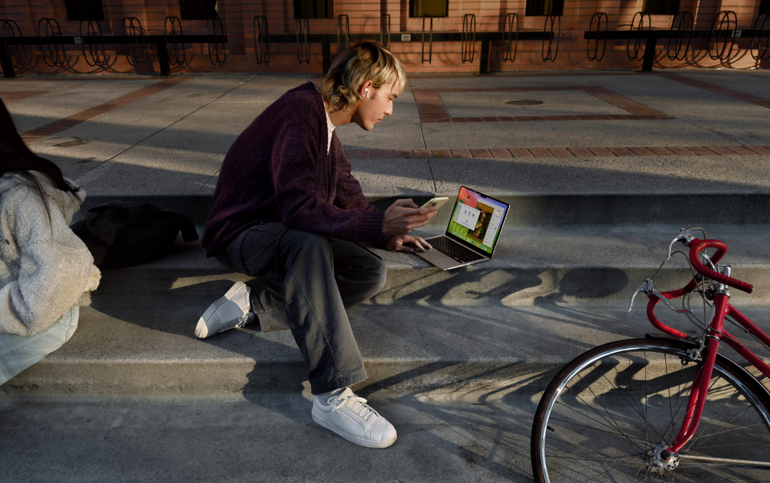 Egy lépcsőn ülő diák iPhone-t és MacBookot használ, mellette egy kerékpár