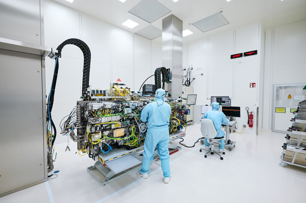 Zwei Techniker:innen bei TRUMPF in Ditzingen in Schutzkleidung in einer laborähnlichen Umgebung neben einer riesigen Maschine.
