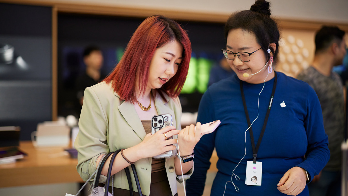 Une cliente qui tient un iPhone 15 rose et discute avec une membre de l’équipe de la boutique Apple Nanjing East.