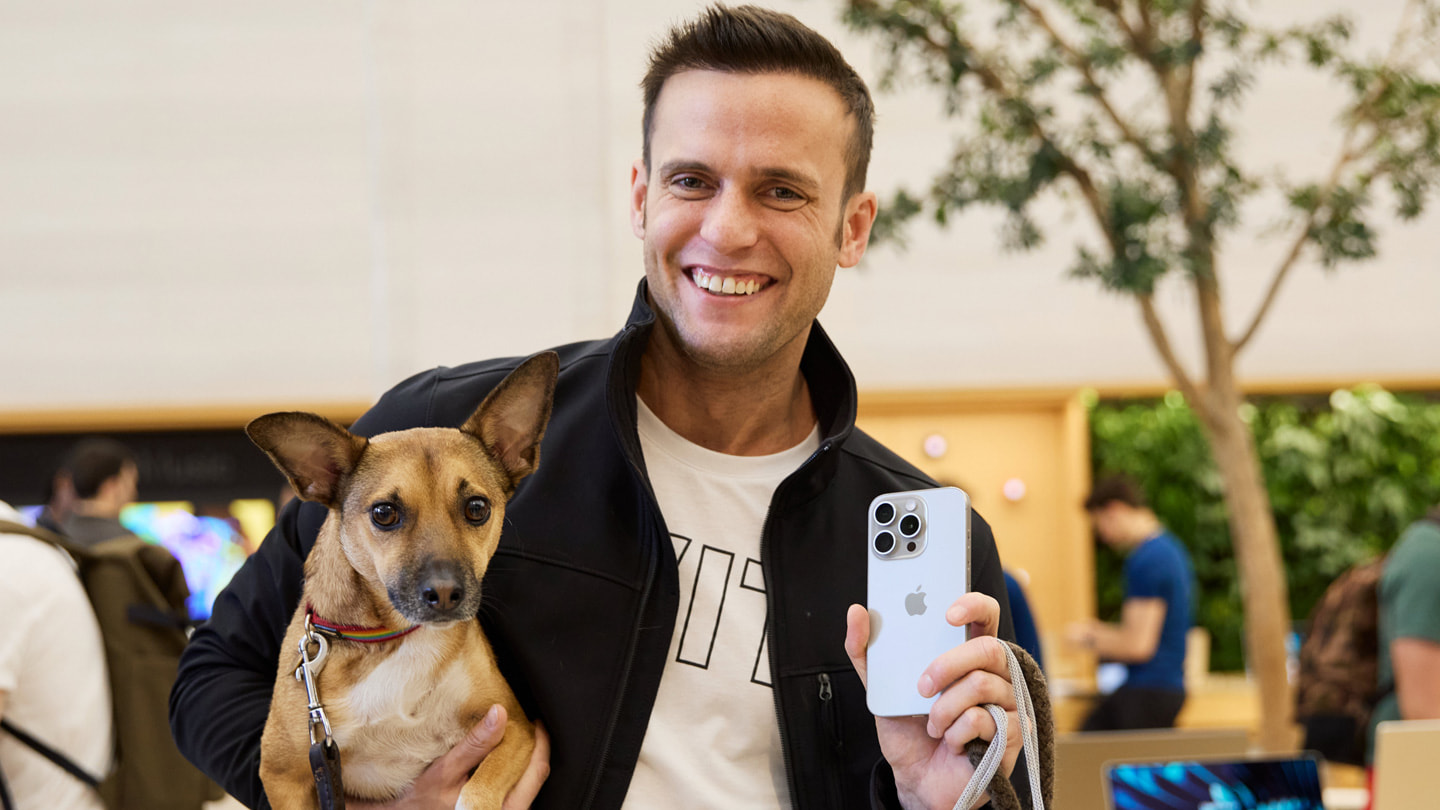Klient trzymający w jednej ręce psa, a w drugiej iPhone’a 15 Pro w kolorze tytanu naturalnego kupionego w sklepie Apple Regent Street w Londynie.