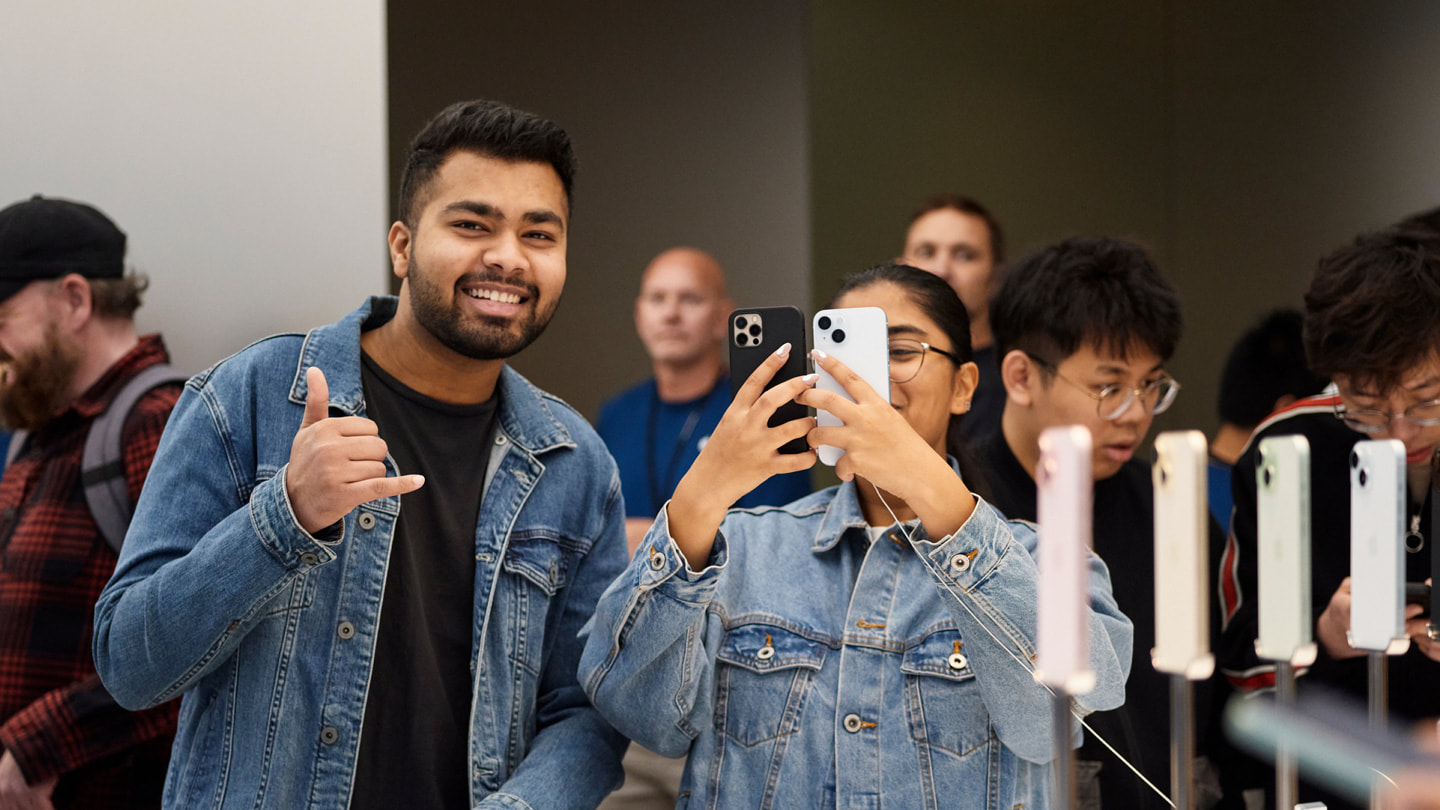 Zwei Kund:innen lachen und halten zwei iPhone Geräte im Apple Sydney, Australien, hoch.