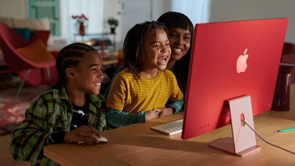 M3 칩을 장착한 새로운 핑크 색상의 iMac과 컬러 매칭 키보드 및 마우스를 사용하고 있는 두 어린이와 부모의 모습.