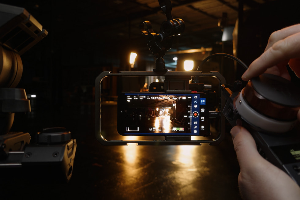 iPhone 15 Pro Max sits on top of a rig on set, capturing a person playing a guitar on a couch.