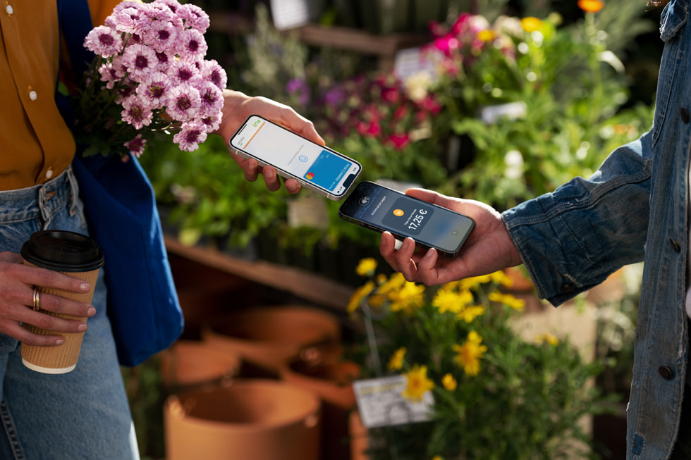 Una persona con un mazzo di fiori in mano che avvicina il suo iPhone a quello dell’esercente per completare una transazione.