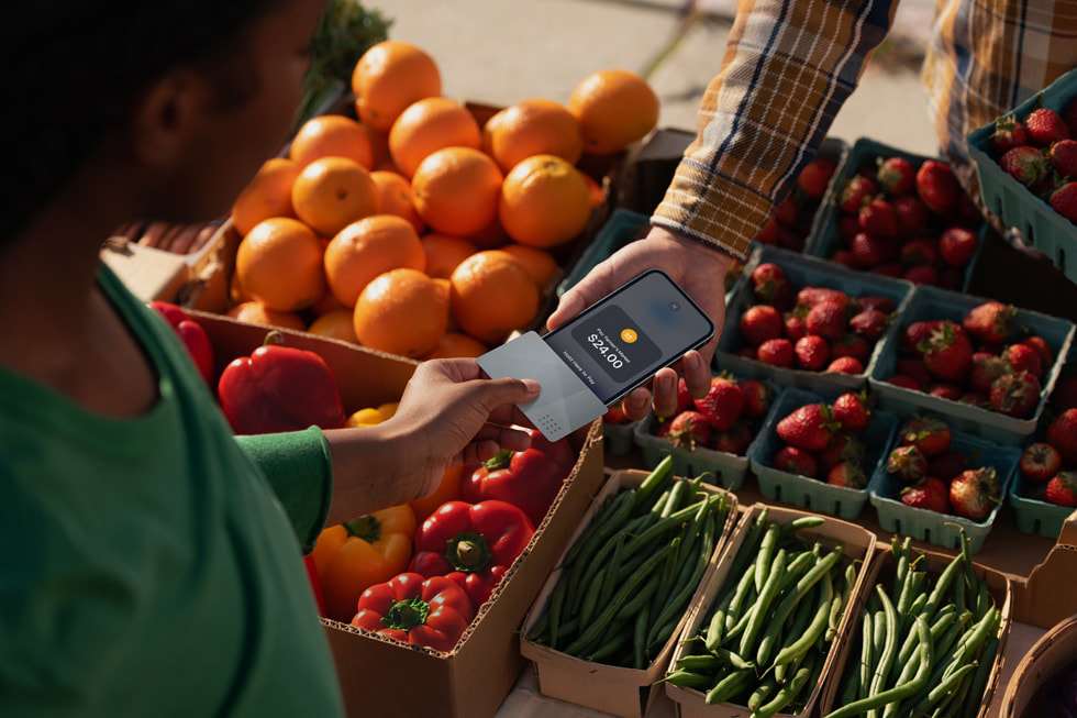 A customer holds their iPhone next to a merchant’s iPhone to complete their transaction in a farmer’s market setting.