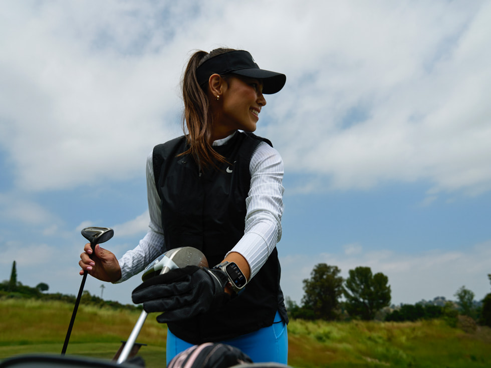 Na obrázku je golfistka s hodinkami Apple Watch držící dvě golfové hole
