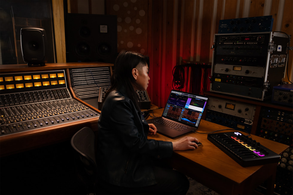 Pengguna Logic Pro diperlihatkan sedang bekerja menggunakan MacBook Pro di studio musik.