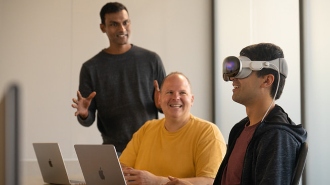 A developer testing out Apple Vision Pro with two other developers watching is shown.
