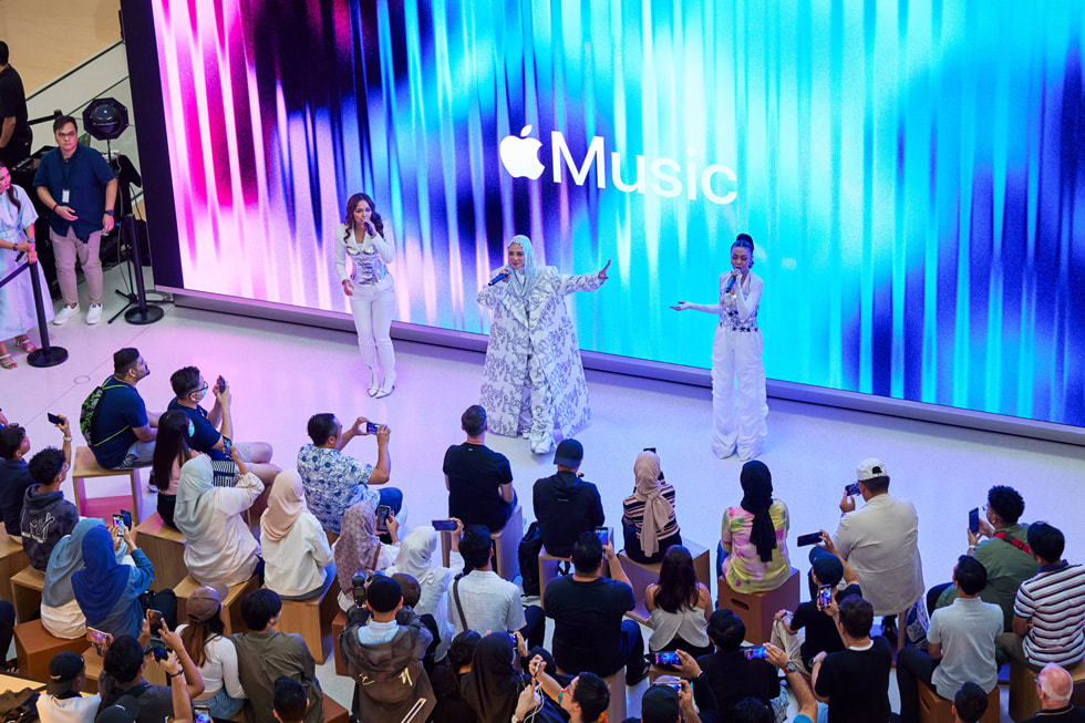 Imagen panorámica de De Fam cantando para los clientes, con el logo de Apple Music en la pantalla de fondo.