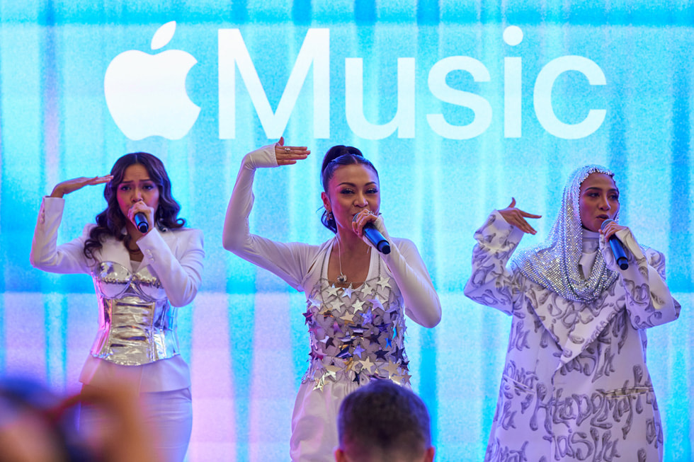 A close-up of De Fam performing, with the Apple Music logo on the screen behind them.