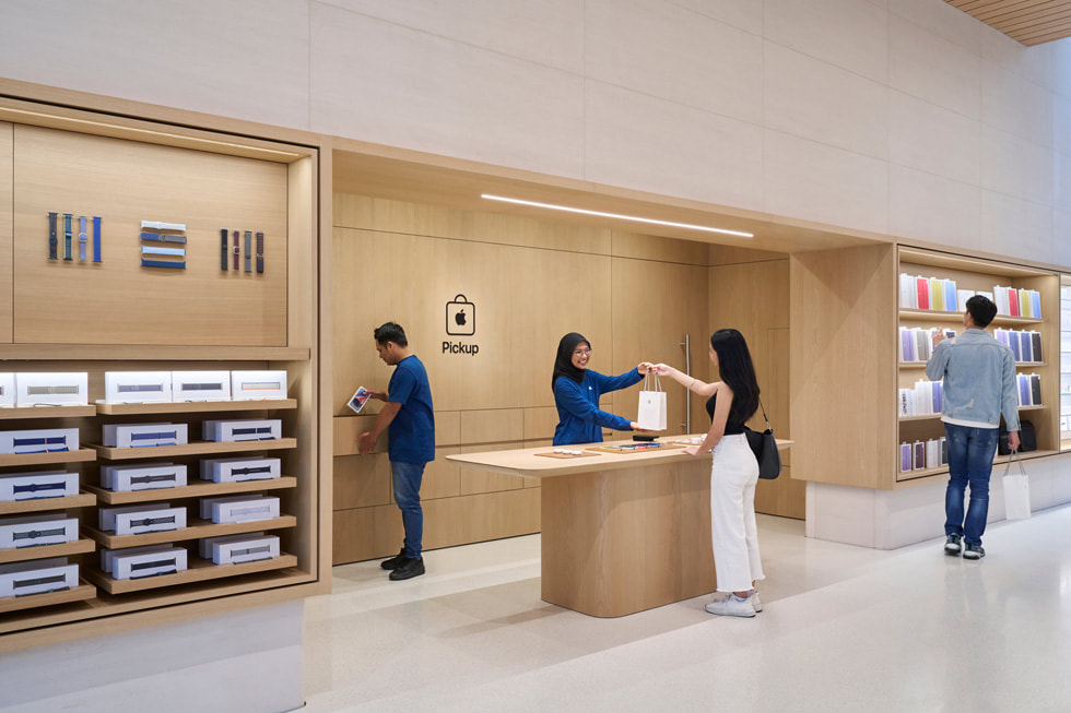 Two team members assist a customer at the Apple Pickup area inside Apple The Exchange TRX.