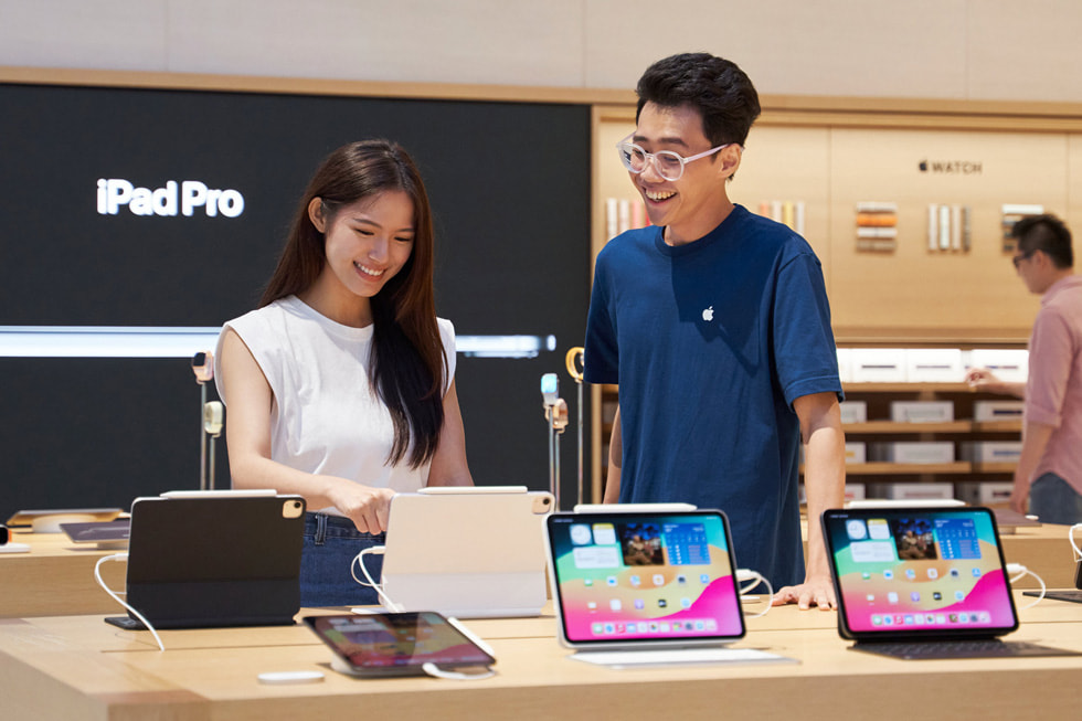Seorang pelanggan dan anggota tim berdiri di depan bidang pajang iPad di toko.