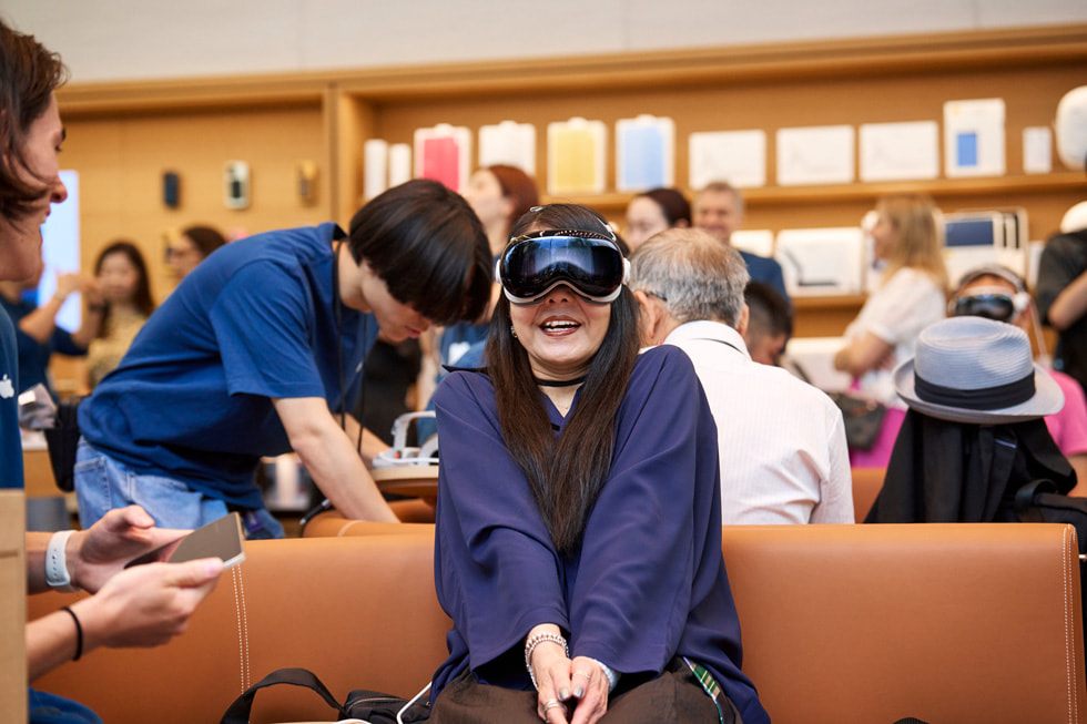 A customer wearing Apple Vision Pro in the Demo Zone in Apple Omotesando smiles and clasps her hands together.