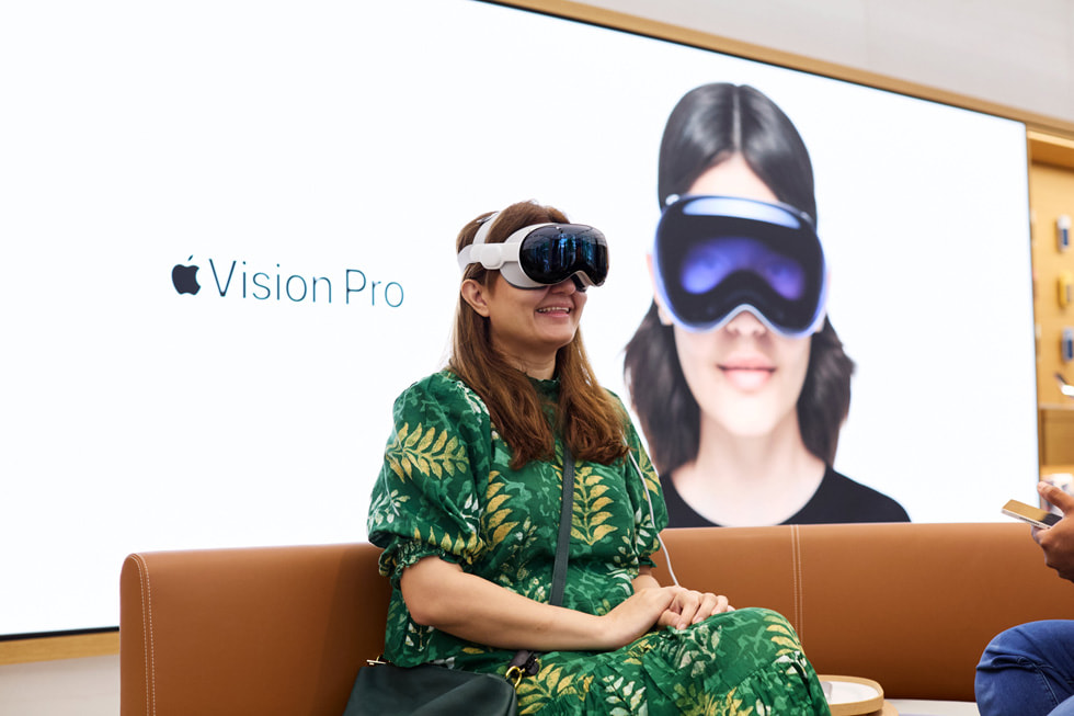 A customer in a green dress takes a seat while wearing Apple Vision Pro.