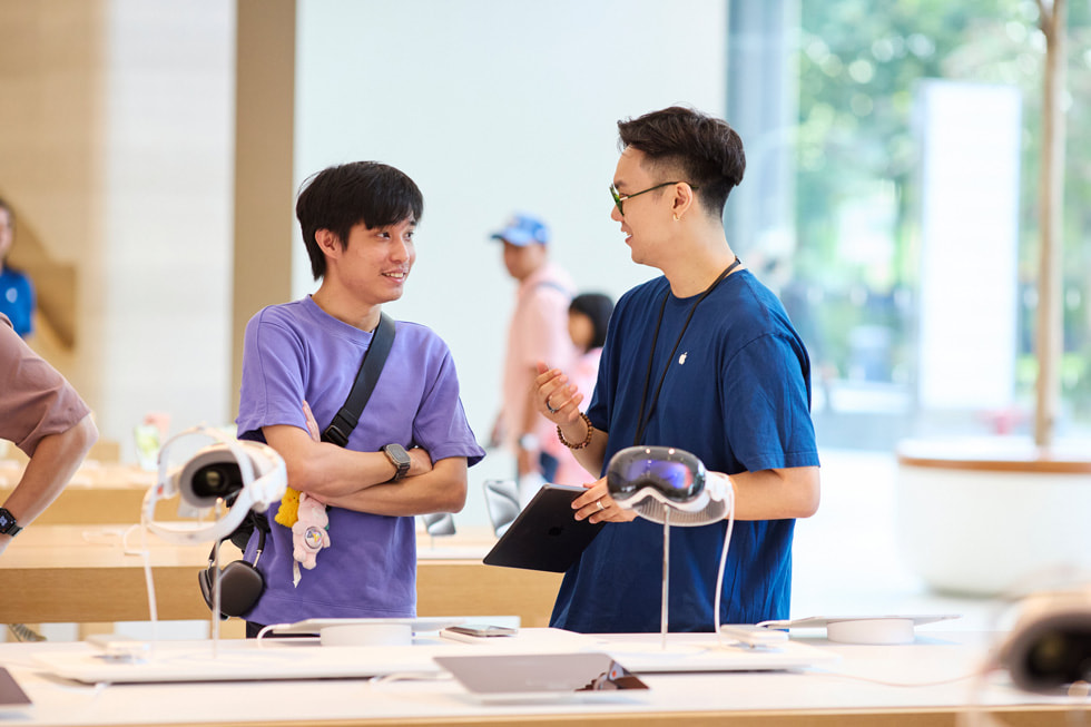 Bir müşteri ve bir ekip üyesi, Apple Vision Pro ekranın arkasında duruyor.