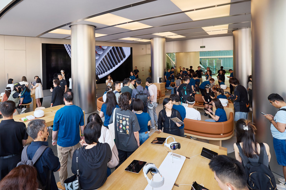 Wangfujing Apple Store'un yakınlaştırılmış bir çekimi, arkadaki demo alanıyla birlikte müşterilerin mağazayı keşfettiğini gösteriyor.