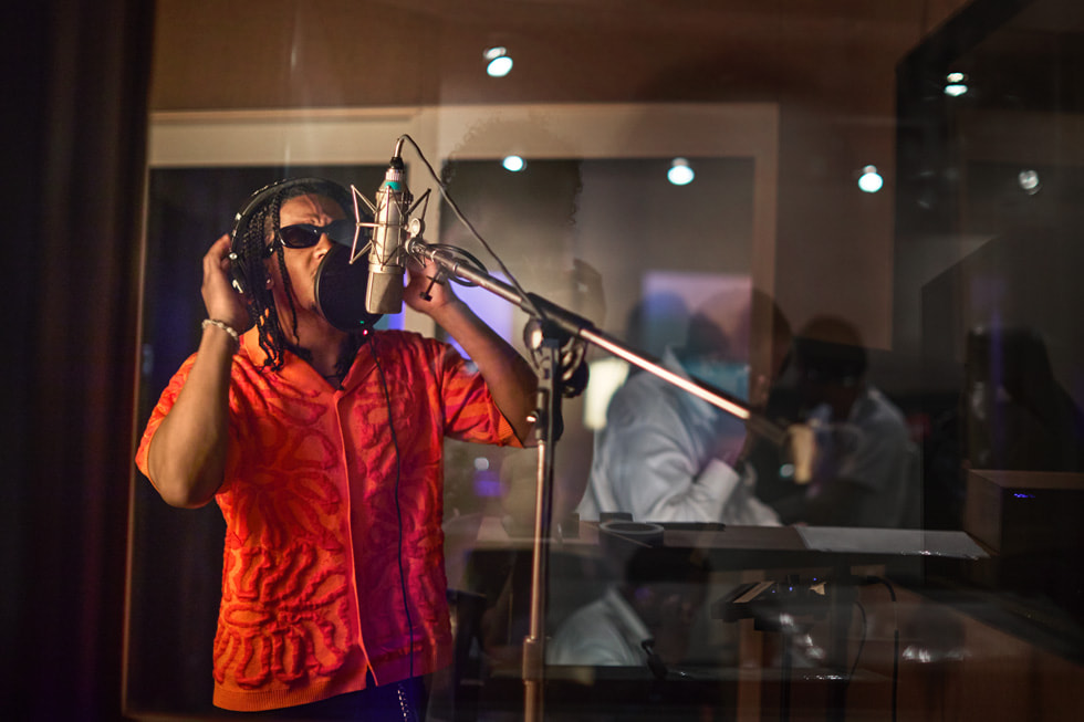 Wearing headphones, Emmanuel Strickland sings into a professional microphone in a studio setting.