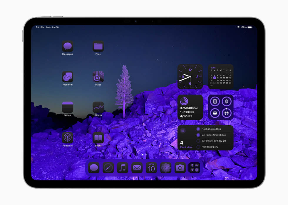 Sur un iPad Pro, les icônes d’apps et les widgets encadrent un fond d’écran constitué d’une image de paysage, le tout baigné d’une teinte violette. 