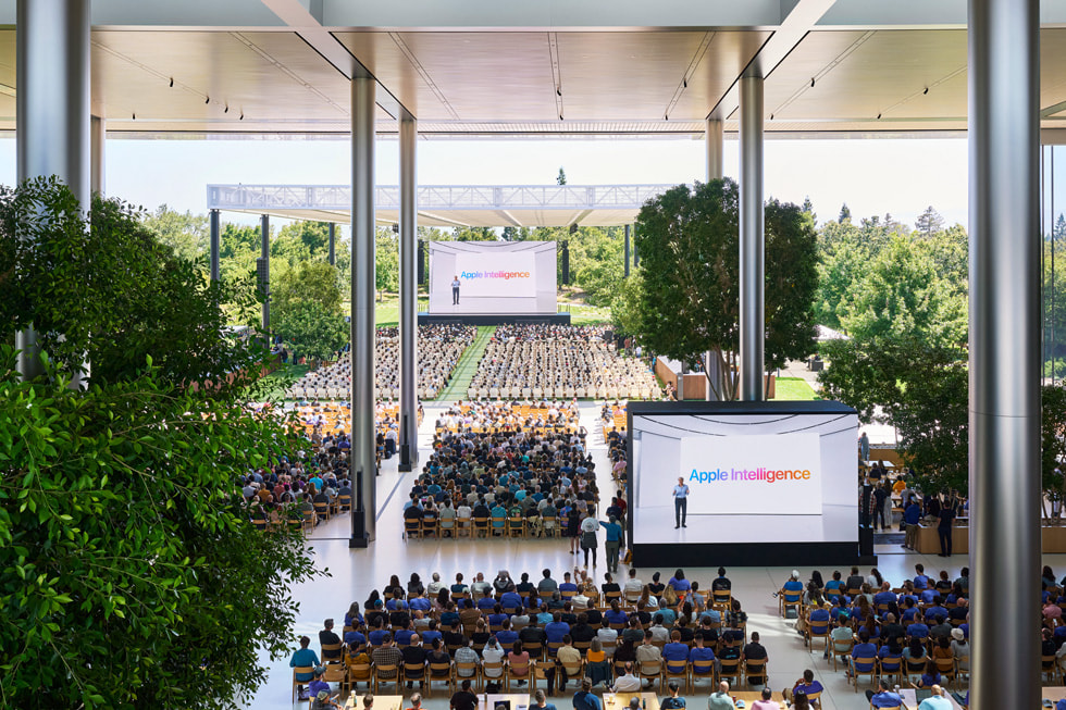 ภาพเหนือศีรษะแสดงให้เห็นนักพัฒนากำลังรับชมการนำเสนอคีย์โน้ตบนหน้าจอขนาดใหญ่ใน Caffè Macs ที่ Apple Park 