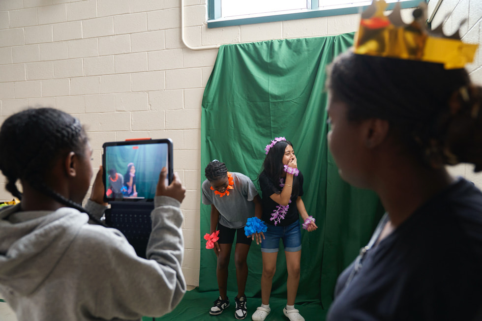 Learners at the STEM Explorers camp pose in front of a green screen while another participant takes their photo on iPad.