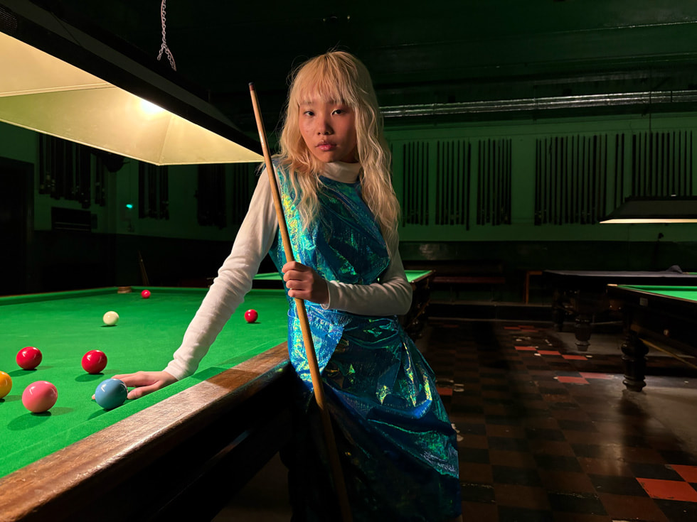 A person poses against a billiards table in a low-light room.