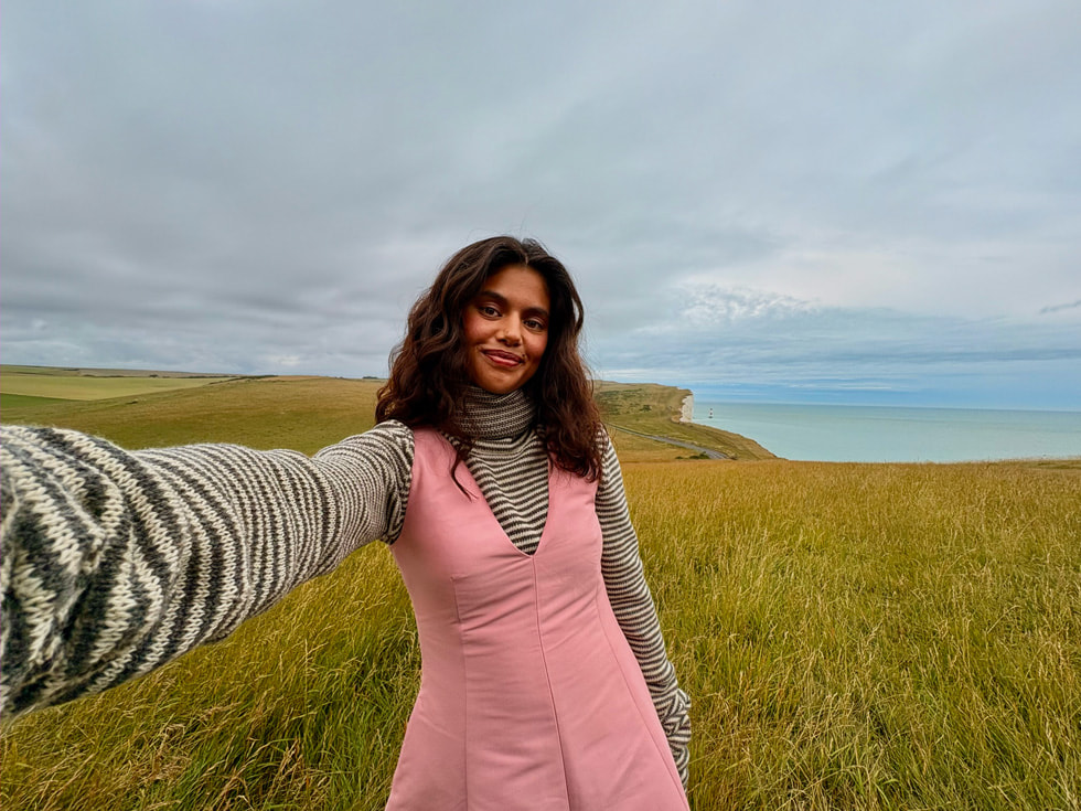 A selfie is shown with a grassy landscape leading to the sea. 